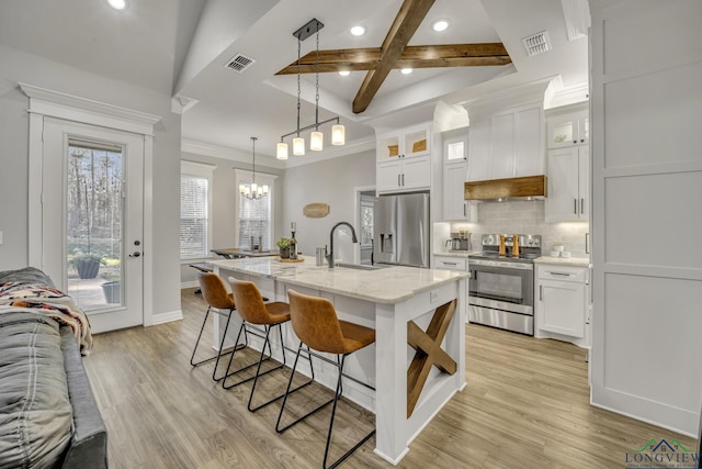 kitchen featuring beam ceiling, stainless steel appliances, an island with sink, and white cabinetry