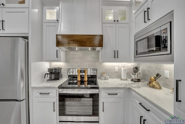 kitchen featuring appliances with stainless steel finishes, light stone countertops, white cabinets, extractor fan, and backsplash