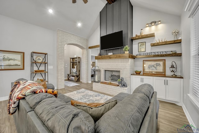 living room with high vaulted ceiling, a brick fireplace, light wood-type flooring, and ceiling fan