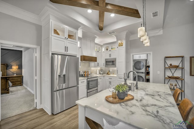 kitchen with stacked washing maching and dryer, appliances with stainless steel finishes, hanging light fixtures, light stone counters, and white cabinetry