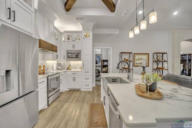 kitchen featuring white cabinets, stainless steel appliances, stacked washing maching and dryer, and beam ceiling