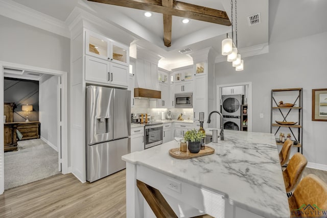 kitchen with appliances with stainless steel finishes, hanging light fixtures, stacked washing maching and dryer, and white cabinetry