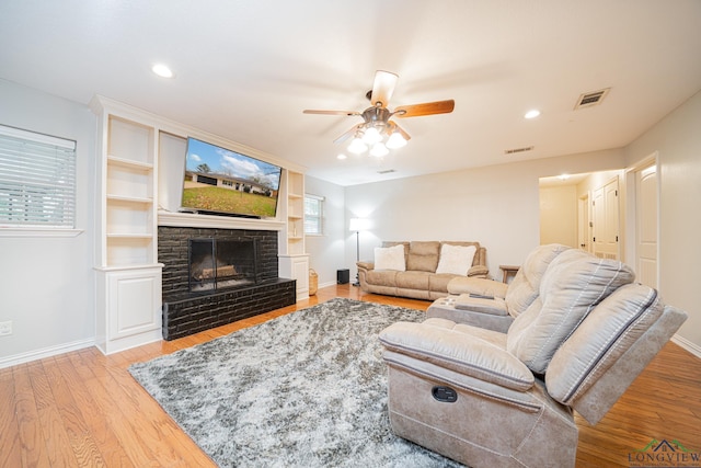 living room with ceiling fan, a stone fireplace, and wood-type flooring