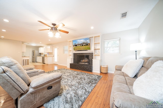 living room featuring a fireplace, ceiling fan, and light hardwood / wood-style flooring