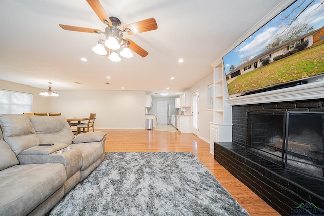 living room with built in shelves, ceiling fan with notable chandelier, and light hardwood / wood-style floors