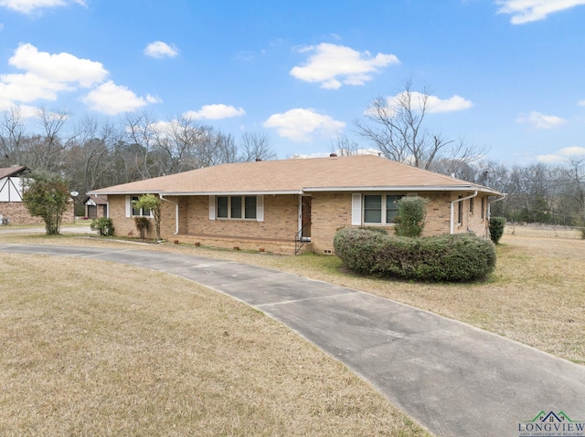 ranch-style house featuring driveway, brick siding, a shingled roof, and a front lawn
