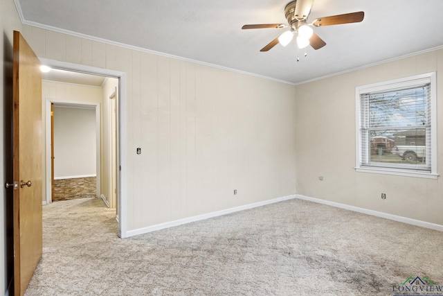 carpeted empty room with wood walls, crown molding, a ceiling fan, and baseboards