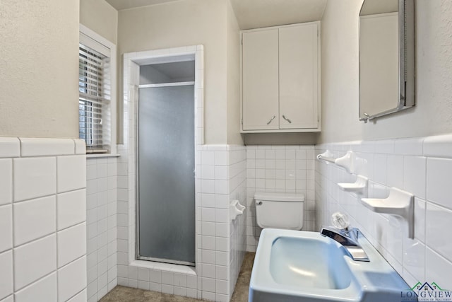 bathroom with tile walls, a sink, a shower stall, toilet, and wainscoting