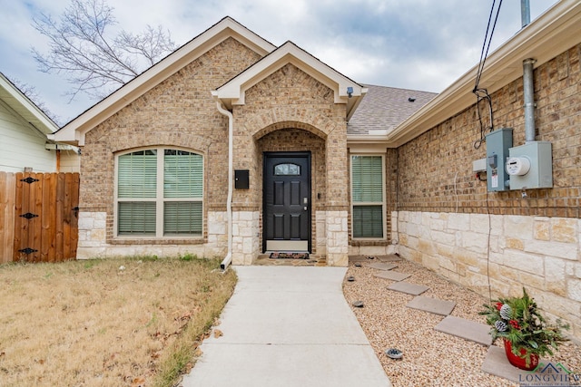 property entrance featuring stone siding, brick siding, roof with shingles, and a gate