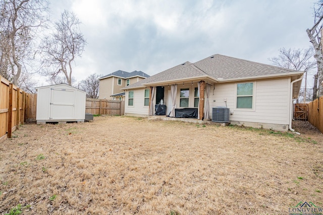 back of property featuring a fenced backyard, roof with shingles, an outbuilding, a storage unit, and central AC