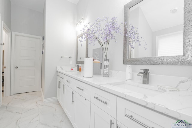 bathroom featuring marble finish floor, double vanity, vaulted ceiling, a sink, and baseboards