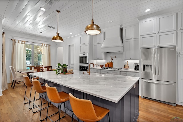 kitchen with stainless steel appliances, a notable chandelier, light wood-style flooring, and premium range hood