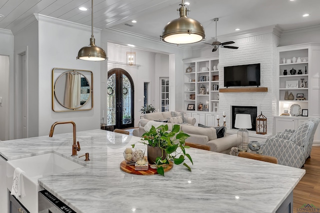 interior space featuring ceiling fan, crown molding, a brick fireplace, built in shelves, and dark wood-style floors