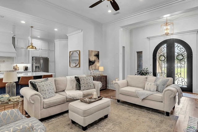 living room with french doors, ceiling fan with notable chandelier, light wood-type flooring, visible vents, and ornamental molding