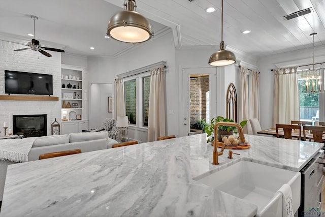 kitchen featuring a sink, pendant lighting, ceiling fan with notable chandelier, and a fireplace