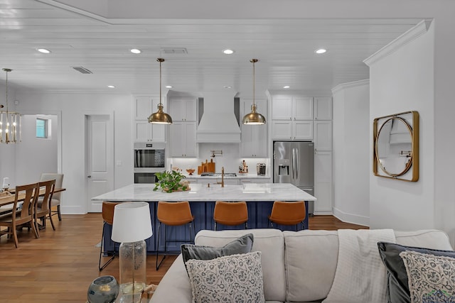 kitchen featuring wood finished floors, open floor plan, premium range hood, a kitchen bar, and stainless steel appliances