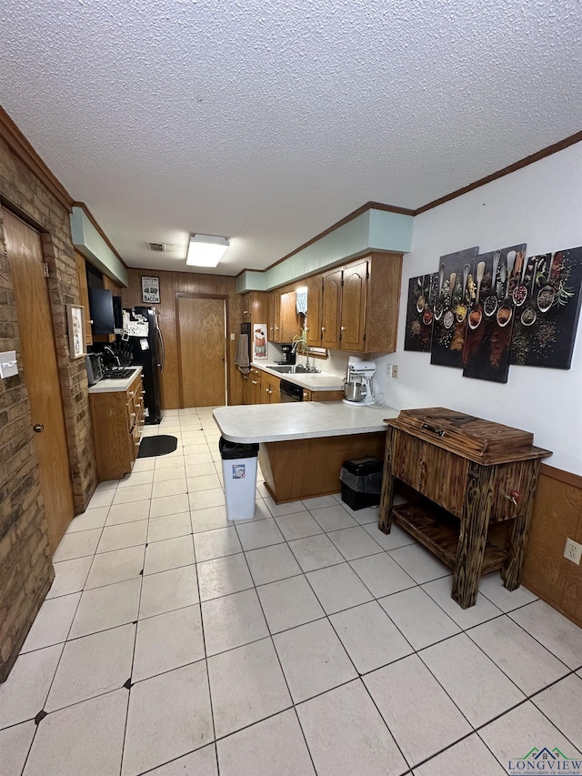 kitchen with kitchen peninsula, a textured ceiling, crown molding, wooden walls, and sink