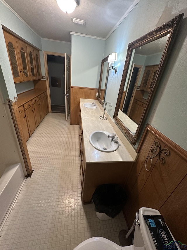 bathroom with wood walls, crown molding, vanity, and a textured ceiling