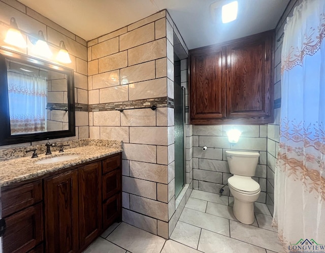 bathroom with a shower, tile walls, vanity, toilet, and tile patterned floors