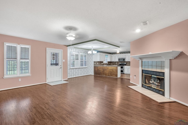 111 E Sycamore Ln, Longview, TX 75604 - unfurnished living room with dark wood-style flooring, a chandelier, a tiled fireplace, and a ceiling fan