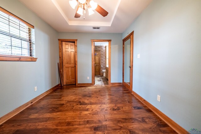 unfurnished bedroom with ensuite bath, ceiling fan, french doors, dark hardwood / wood-style floors, and a tray ceiling