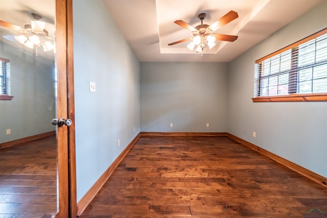 unfurnished room with a raised ceiling, ceiling fan, and dark wood-type flooring