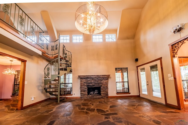 unfurnished living room featuring a notable chandelier, a stone fireplace, a high ceiling, and french doors