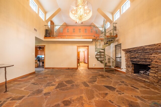 unfurnished living room with plenty of natural light, a fireplace, ceiling fan with notable chandelier, and a high ceiling