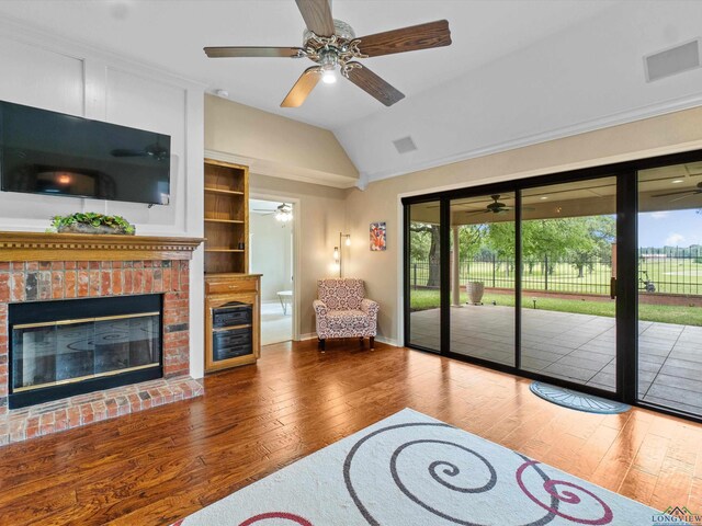 living area with ceiling fan, wood-type flooring, lofted ceiling, and a brick fireplace