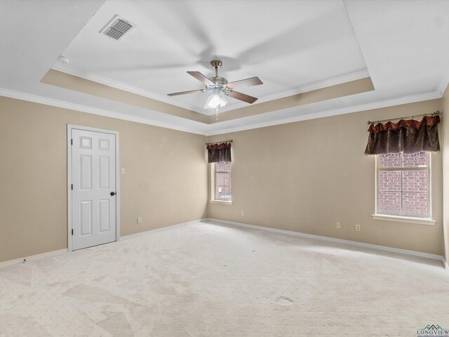empty room with visible vents, ceiling fan, a tray ceiling, baseboards, and ornamental molding