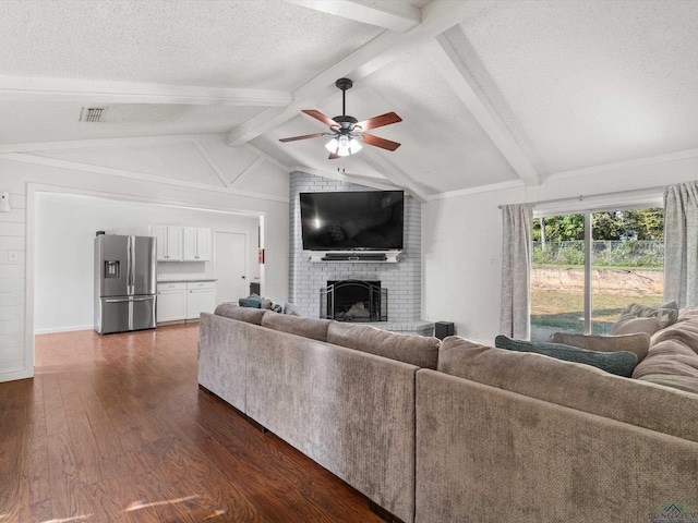 living room with ceiling fan, dark wood-type flooring, lofted ceiling with beams, a textured ceiling, and a fireplace