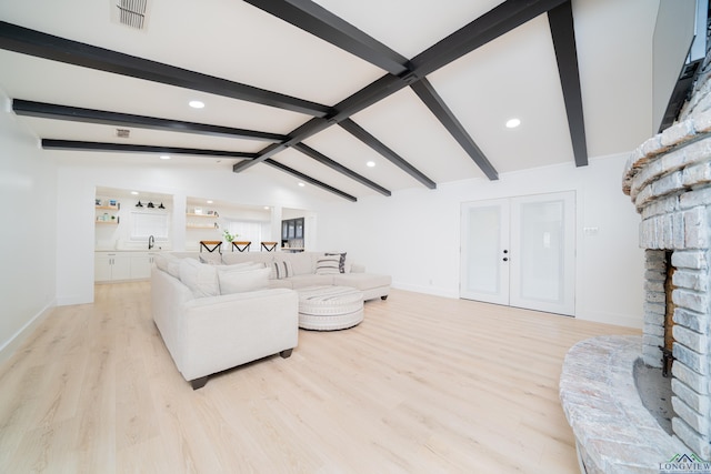 living area with lofted ceiling with beams, a fireplace with raised hearth, light wood-type flooring, and visible vents