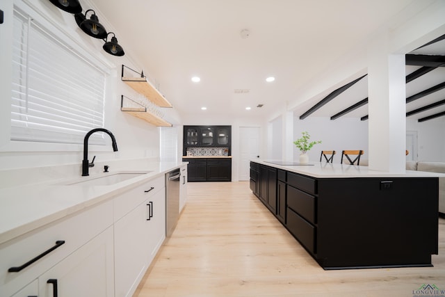 kitchen with a kitchen island, dark cabinets, light countertops, white cabinetry, and a sink