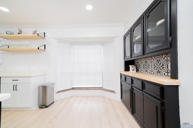 kitchen featuring glass insert cabinets, ornamental molding, light countertops, and dark cabinetry