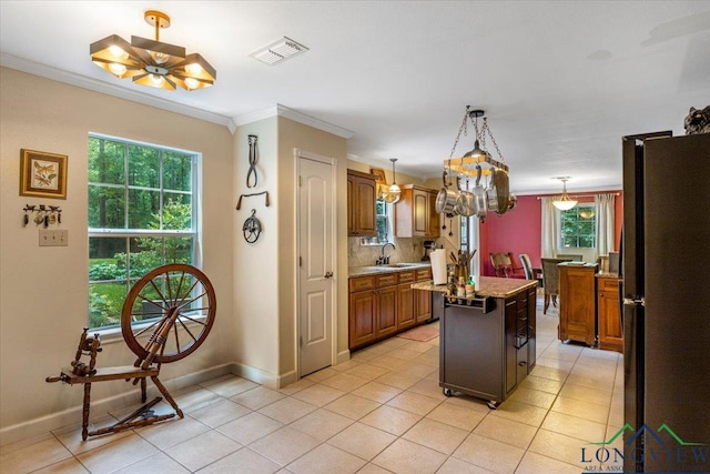 kitchen featuring freestanding refrigerator, a chandelier, crown molding, a center island, and brown cabinets