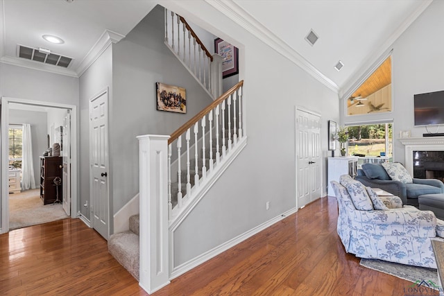 staircase with wood-type flooring, a premium fireplace, ornamental molding, and high vaulted ceiling