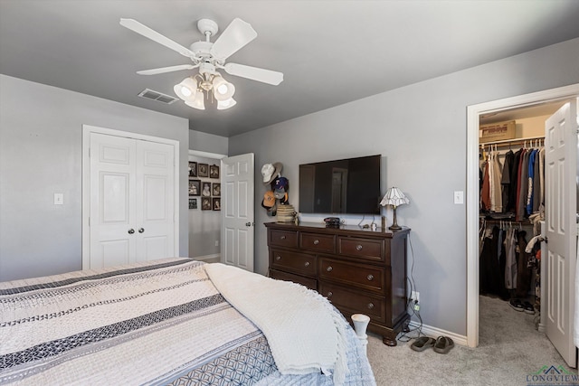 carpeted bedroom with a walk in closet and ceiling fan