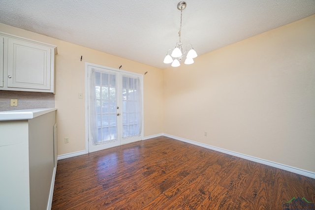 unfurnished dining area with french doors, a textured ceiling, dark wood-type flooring, and a notable chandelier