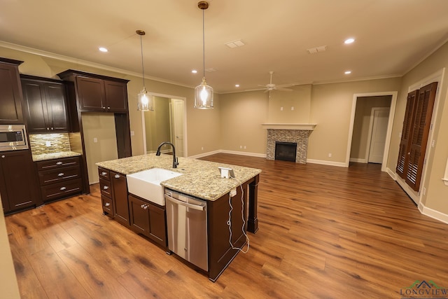 kitchen with ceiling fan, sink, stainless steel appliances, light stone counters, and a tiled fireplace