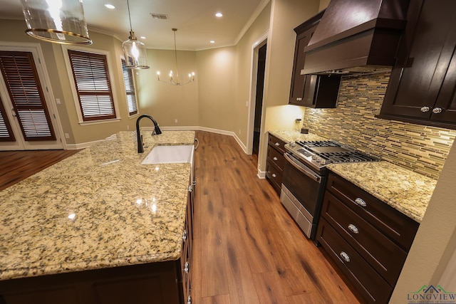 kitchen with light stone countertops, custom range hood, sink, pendant lighting, and stainless steel range with gas stovetop