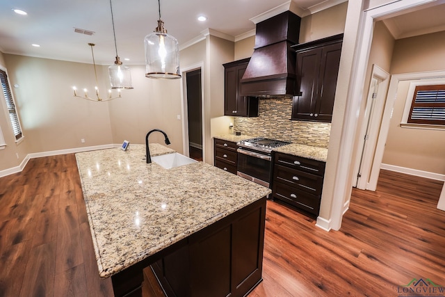 kitchen with sink, a large island with sink, decorative light fixtures, custom range hood, and stainless steel range with gas stovetop