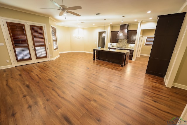 kitchen with pendant lighting, backsplash, premium range hood, a center island with sink, and sink