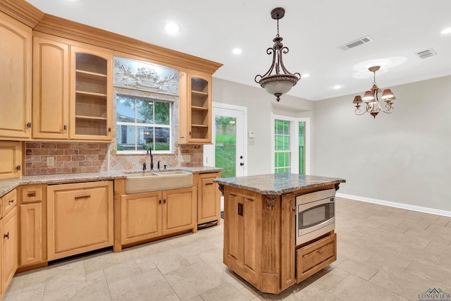 kitchen featuring stainless steel microwave, sink, tasteful backsplash, light stone counters, and pendant lighting