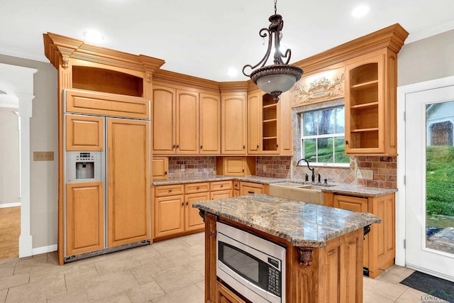 kitchen with light stone countertops, backsplash, pendant lighting, built in appliances, and a center island