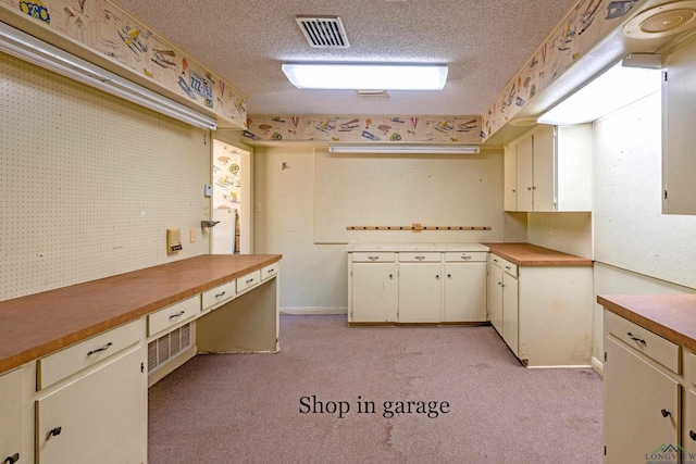 kitchen featuring light carpet, cream cabinets, and a textured ceiling