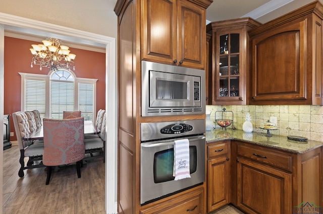 kitchen featuring backsplash, brown cabinetry, appliances with stainless steel finishes, and a chandelier