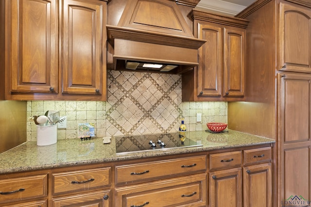 kitchen with custom exhaust hood, backsplash, brown cabinetry, and black electric stovetop