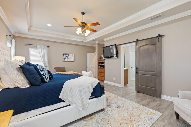 bedroom featuring visible vents, a tray ceiling, a barn door, crown molding, and light wood finished floors