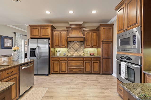 kitchen with decorative backsplash, stone countertops, premium range hood, and appliances with stainless steel finishes