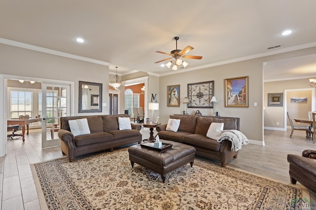 living area with light wood finished floors, visible vents, baseboards, ornamental molding, and ceiling fan with notable chandelier